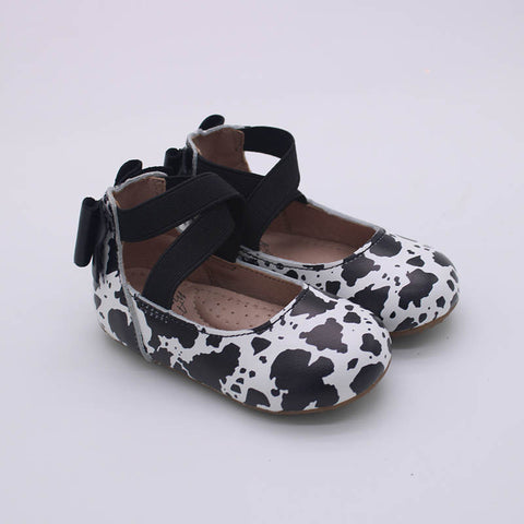 Girls boutique cow print leather ballet shoe with a black bow back.